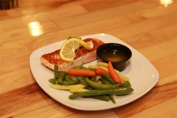 Grilled Salmon with lemon on top and a side of mixed vegetables and butter.