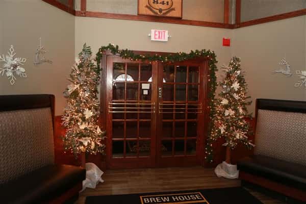 Double doors inside the restaurant that is aligned with garland and lights with one decorated Christmas tree on each side.