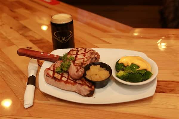 Steak with a side of broccoli on a white plate with a dark beer on a wooden table.