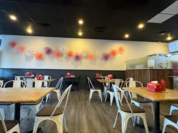 Restaurant dining room with tables and metal chairs, ceiling lights, and a decorative wall display.