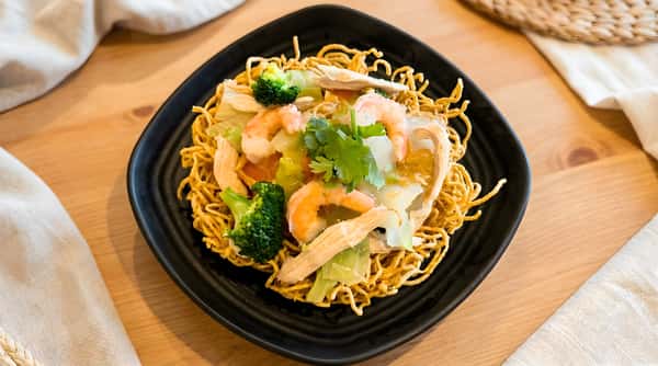 Crispy noodle stir fry in a takeout bowl topped with shrimp, vegetables, and herbs.