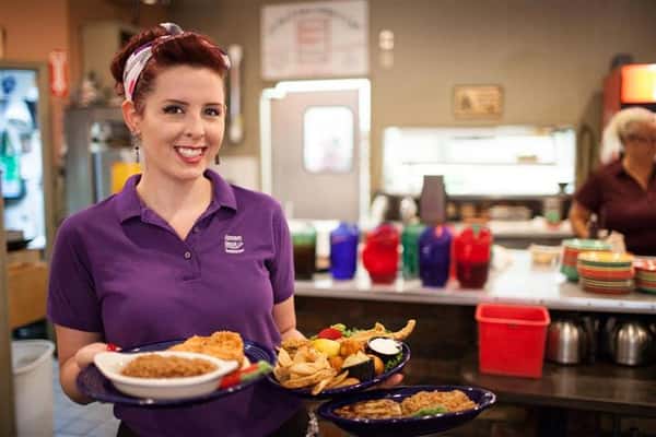 waitress smiling at the camera holding various dinner dishes