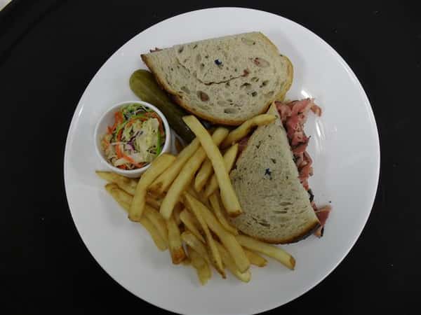 sandwich with roast beef and a side of french fries and cole slaw and pickle spear