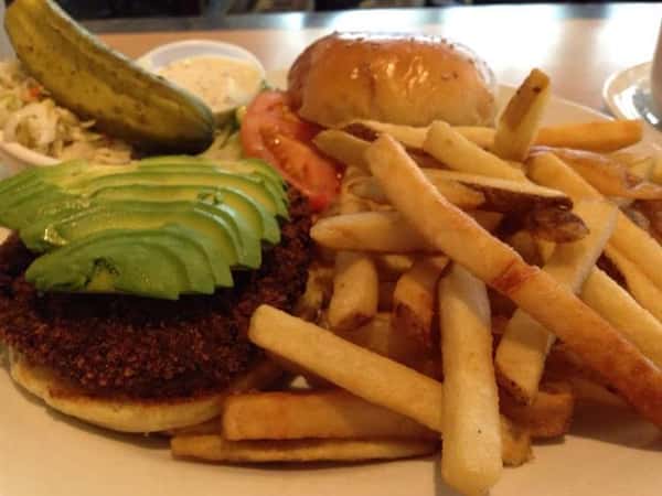 hamburger topped with avocado slices, tomao slice and a side of french fries and a pickle spear