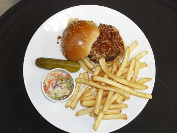 hamburger topped with bacon and cheese with a side of french fries, cole slaw and a pickle spear