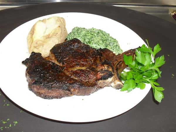 cooked steak with a side of creamed spinach and baked potato
