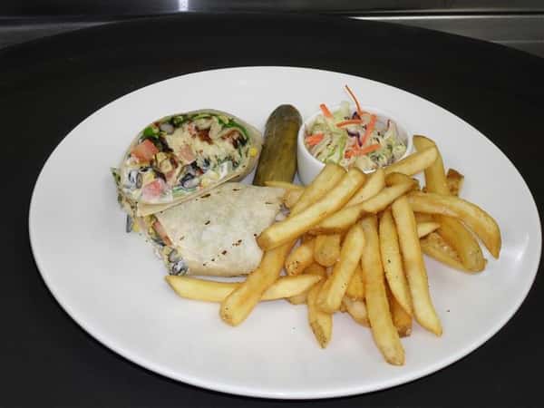 wrap with a variety of ingredients, a side of french fries, cole slaw and a pickle spear