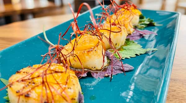 Seared scallops topped with saffron threads and citrus zest, served on green and purple leaves on a teal plate.