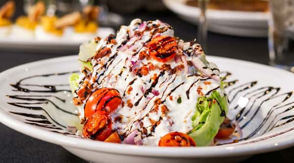 Wedge salad with blue cheese dressing, cherry tomatoes, red onion, bacon, and balsamic glaze.