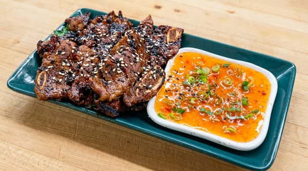 Kalbi short ribs with sesame seeds and a side of orange dipping sauce with green onions.