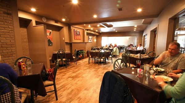 Restaurant interior with wooden floors, brown walls, art, and diners seated at dark tables.