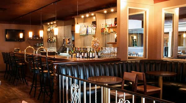 Dimly lit bar with a long wooden counter, bar stools, bottles of liquor, and booth seating.