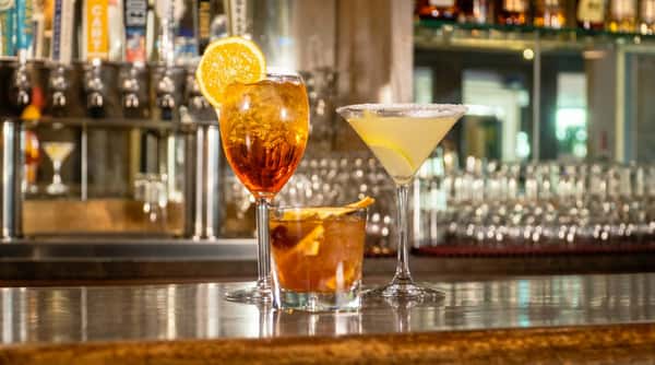 Three cocktails on a bar: a spritz with an orange slice, a margarita, and an old fashioned.
