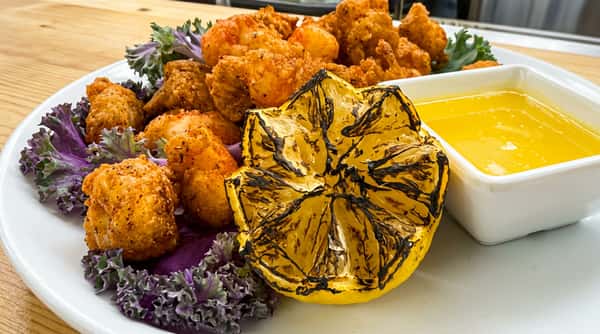 Fried shrimp on a bed of purple kale, with a charred lemon half and a side of butter sauce.