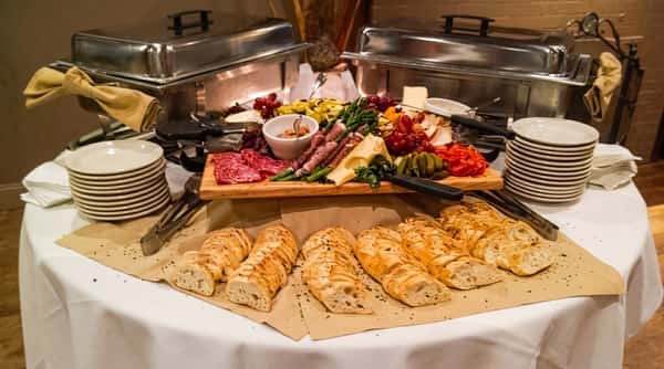 A buffet table with a charcuterie board of meats, cheeses, grapes, vegetables, and baguettes.