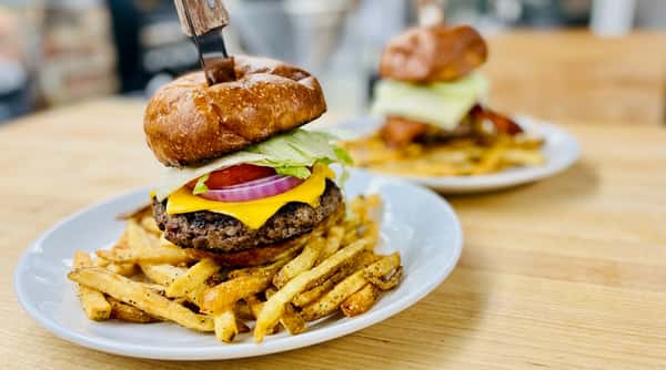 Cheeseburger with lettuce, tomato, and red onion, skewered with a knife, served with french fries.