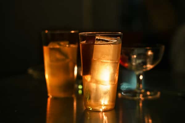 Chilled whiskey cocktails with large ice cubes glowing under warm ambient lighting, set on a reflective surface.