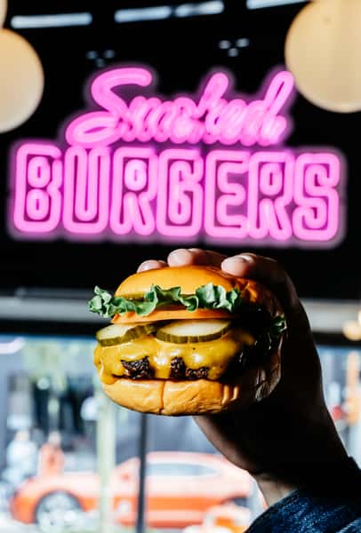 Closeup of cheeseburger in front of neon sign