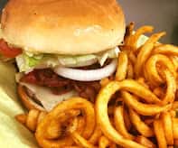 A sandwich with lettuce, tomato, onion, and bacon, served with curly fries.