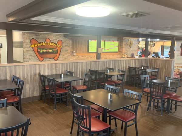Spacious casual restaurant with black tables, red-cushioned chairs, a "Wanna Burger?" mural, and a counter where two people are ordering.