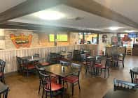 Casual dining area with wooden walls, red-cushioned chairs, and a sign reading "Chilangos" on the wall.