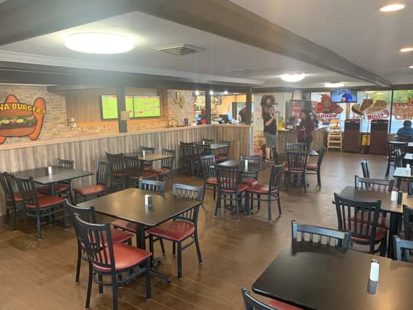 Spacious casual restaurant with black tables, red-cushioned chairs, a "Wanna Burger?" mural, and a counter where two people are ordering.