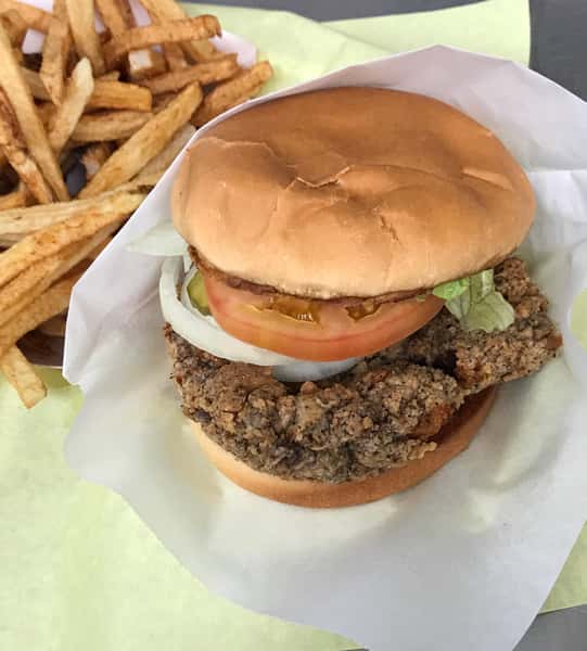 Crispy fried chicken sandwich with lettuce, tomato, onions, and pickles on a bun, served with a side of golden French fries.