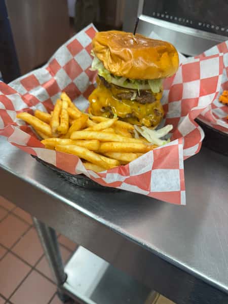 A large cheeseburger with two beef patties, melted cheese, lettuce, and onions, served with crinkle-cut fries in a basket.