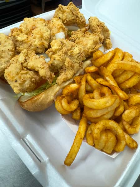 A box of fried chicken tenders on a sandwich bun with lettuce, paired with seasoned curly fries.