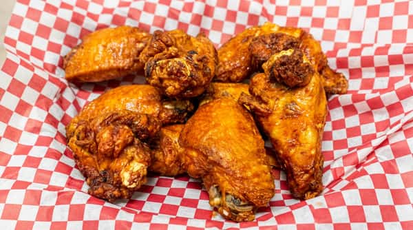 Roasted chicken pieces with crispy brown skin on red and white checkered paper.