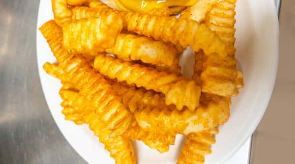Close-up of golden-brown crinkle-cut fries on a white plate.