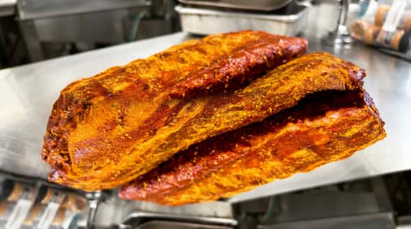 Pork ribs heavily seasoned with an orange-brown dry rub in a metal pan, close-up.