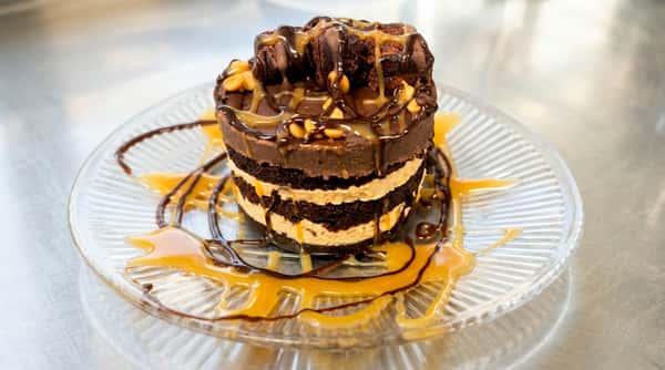 Layered chocolate cake with white frosting, topped with chocolate sauce, caramel, and peanuts.