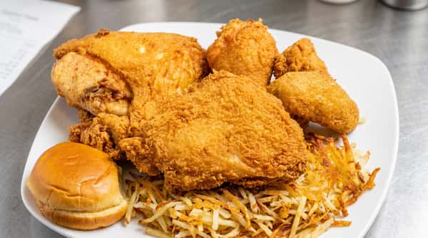 Crispy fried chicken pieces served on a white plate, with what appears to be hash browns and a bun.