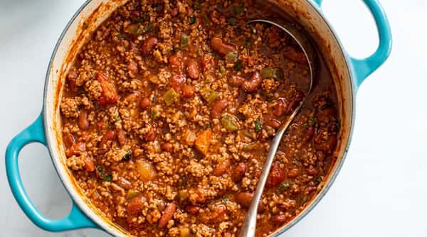 Chili with ground meat, red beans, and chopped vegetables simmering in a large pot with a ladle.