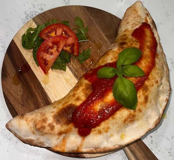 Folded calzone with tomato sauce and fresh basil on a wooden board, served with sliced tomatoes and arugula