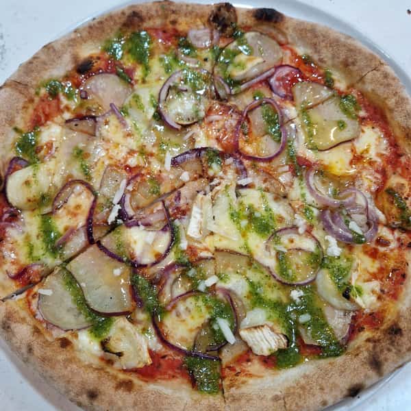 Wood-fired vegetable pizza topped with potatoes, red onions, cheese, and pesto drizzle on a crispy crust