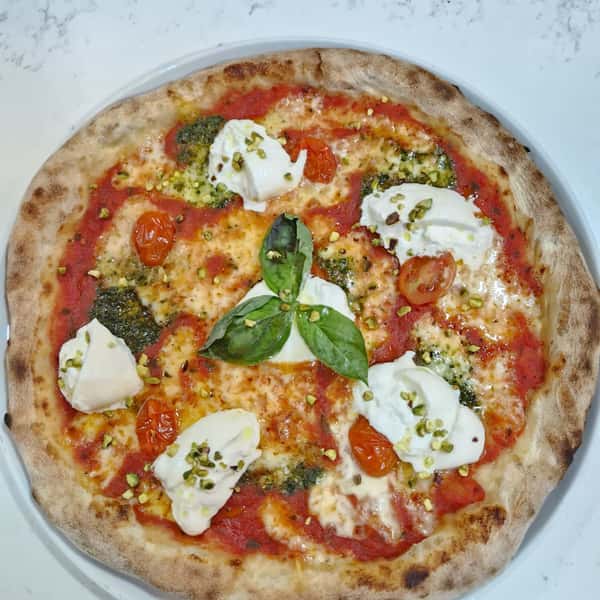Gourmet pizza with tomato sauce, burrata, cherry tomatoes, pesto, and crushed pistachios on a blistered crust