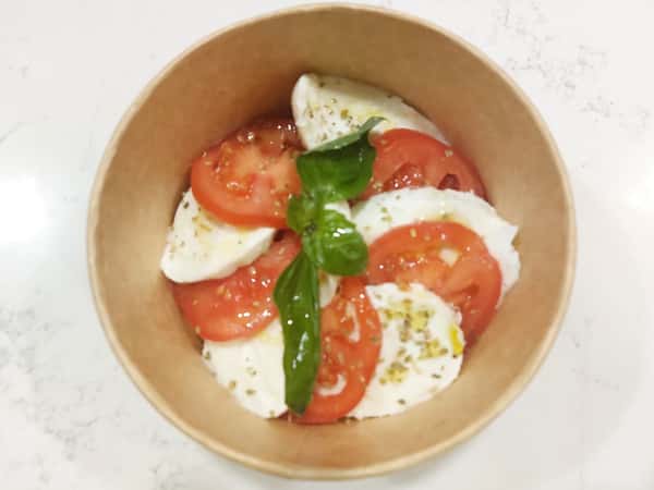 Caprese salad with fresh mozzarella, sliced tomatoes, basil, and olive oil in a takeaway bowl