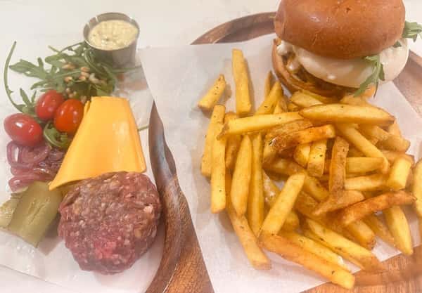 Gourmet burger with melted cheese and arugula served with crispy fries, alongside raw ingredients and house sauce