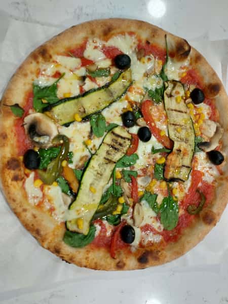 Wood-fired vegetable pizza with grilled zucchini, mushrooms, olives, corn, and fresh greens on a crispy crust