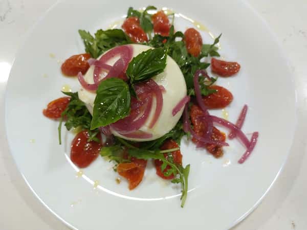 Burrata salad with cherry tomatoes, arugula, pickled red onions, and basil drizzled with olive oil