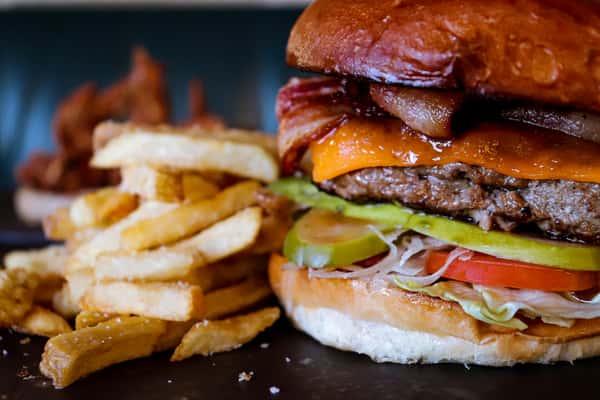 Juicy bacon cheeseburger stacked with cheddar, pickles, lettuce, and tomato on a toasted brioche bun, served with thick-cut golden fries — classic American diner fare.
