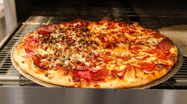Large pizza with pepperoni, ham, and ground sausage, baked in an oven.