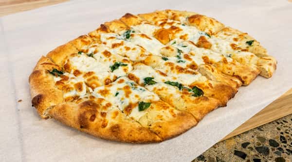Garlic bread with melted mozzarella cheese and spinach on parchment paper.