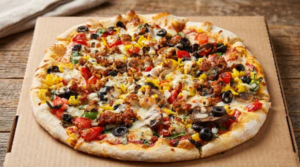 Pizza in a cardboard box, with sausage, black olives, bell peppers, tomatoes, mushrooms, spinach, and melted cheese.