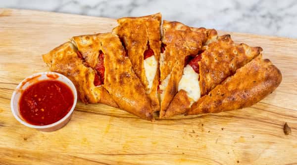 Pepperoni stromboli, sliced open to show melted cheese, served with a side of red sauce on a wooden cutting board.