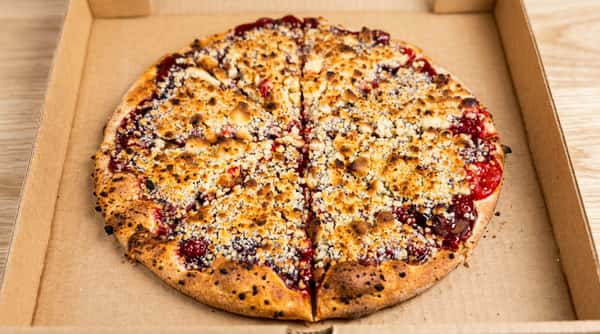 Dessert pizza with fruit topping and cookie crumble, cut into slices in a cardboard box.