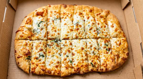Cheesy breadsticks with visible herbs, cut into slices and served in a cardboard pizza box.