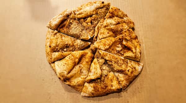Cinnamon dessert pizza, sliced into triangles, with granulated topping and scattered crumbs on a cardboard box.